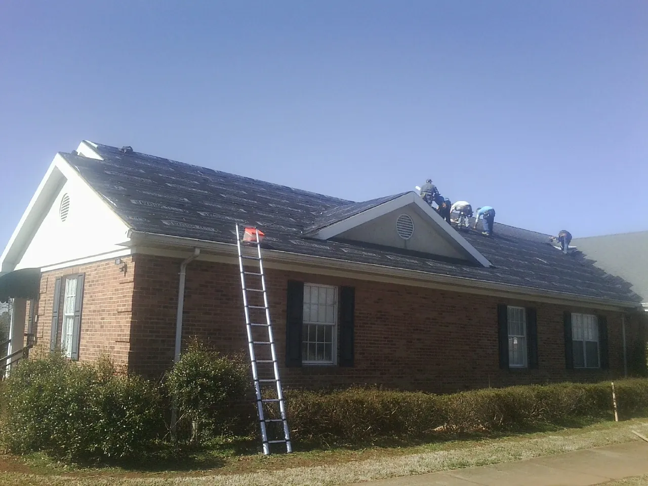 Crew tearing shingles off a brick ranch roof with a ladder set — Metal Roof Repair work by our crew in Randall