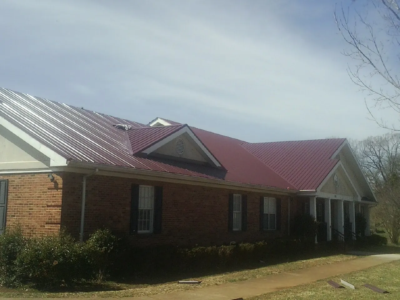Red metal roof with gabled entries on a long brick building, from a Hail Damage Roof Repair job in Randall