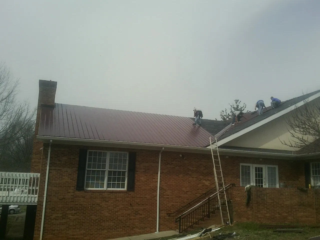 Crew setting red metal roofing panels on a brick home in Randall