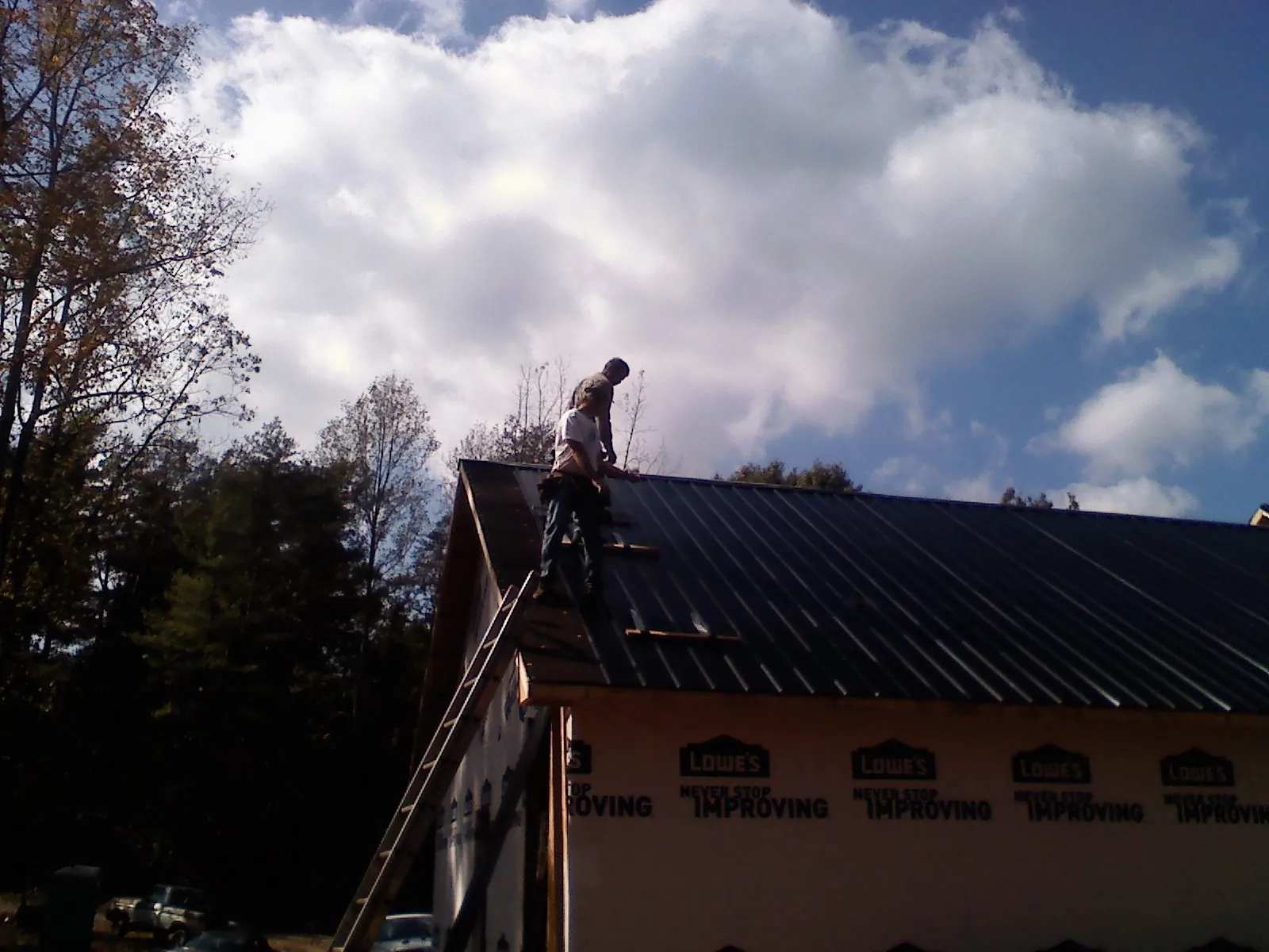 Roofer fastening dark metal panels high against a cloudy sky, from a Roof Inspection job in Randall